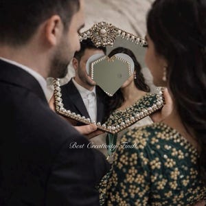 May include: A decorative mirror with a heart-shaped cutout, framed with pearls and gold accents. The mirror reflects a couple, with the text "Best Creativity Finds" visible.