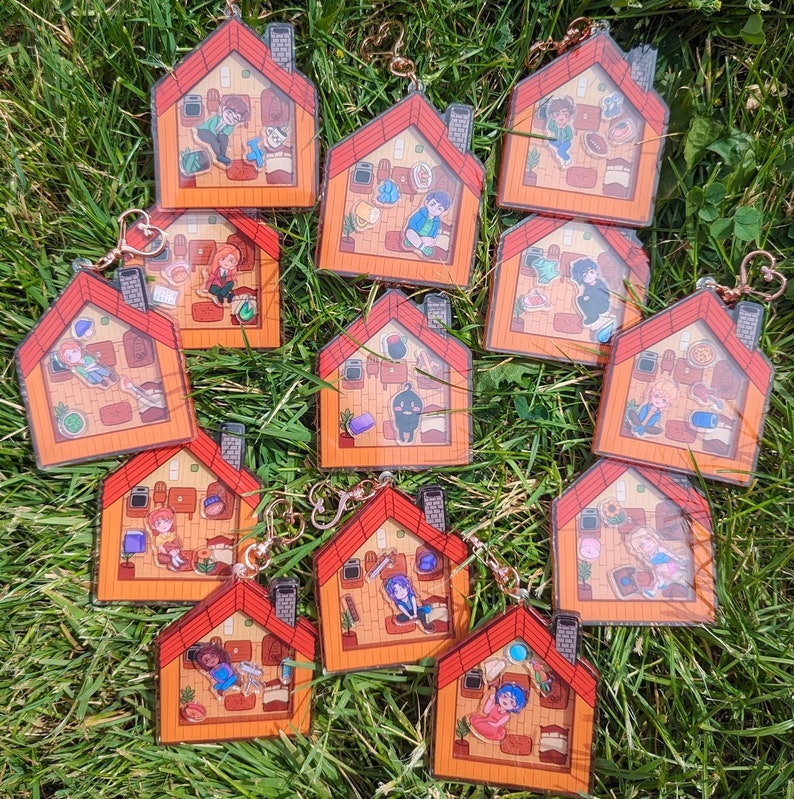 Op de afbeelding: Een set van 11 kleurrijke, ge&iuml;llustreerde sleutelhangers met verschillende personages in een huiselijke setting. Elke sleutelhanger is gemaakt van helder acryl en heeft een metalen ring om aan sleutels of tassen te bevestigen.