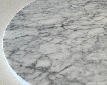 May include: A round, white marble serving tray with gray veining. The tray is smooth and polished.