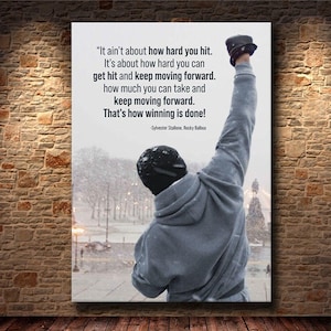 May include: A framed print featuring a quote from Sylvester Stallone's Rocky Balboa, with a figure raising their arm in victory. The quote reads, "It ain't about how hard you hit... That's how winning is done!" The background shows a snowy scene.