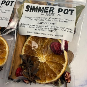May include: A clear plastic pouch labeled SIMMER POT by MARK + Co containing dried orange slices, cranberries, cinnamon sticks, cloves, nutmeg, star anise, and bay leaves. The label includes directions to add contents to 4-6 cups of water.