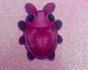 May include: A pink bug sticker with a heart-shaped design and a purple outline. The bug has black eyes and a smiling mouth.
