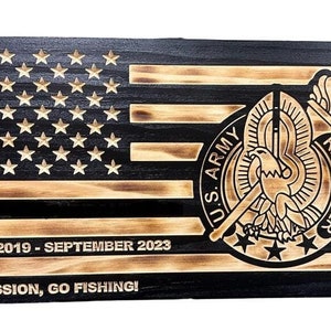 May include: A wooden American flag with a burnt wood finish. The flag has a U.S. Army Recruiter logo in the center. The text "SFC", "AUGUST 2019 - SEPTEMBER 2023", and "MAKE MISSION, GO FISHING!" is also on the flag.