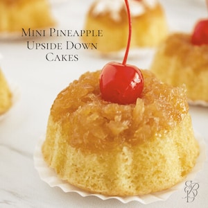 Può includere: Mini torte all'ananas rovesciate. Piccole torte dorate ricoperte di ananas caramellata e una ciliegia rossa brillante. Le torte sono in pirottini di carta bianca, con il testo "Mini Pineapple Upside Down Cakes" sullo sfondo.