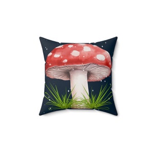 Puede incluir: Cojín cuadrado con una ilustración de acuarela de una seta roja con puntos blancos, sobre un fondo azul oscuro con estrellas. Hierba verde en la base de la seta. Un elemento decorativo para cualquier habitación.