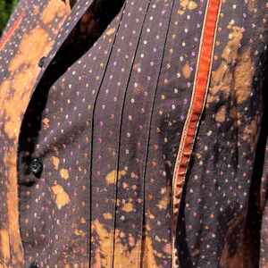 Puede incluir: Una camisa marr&oacute;n de botones con un estampado de lunares blancos y rosas. La camisa tiene un ribete rojo y naranja a lo largo del lado derecho.