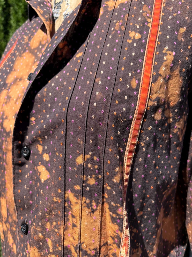 Puede incluir: Una camisa marr&oacute;n de botones con un estampado de lunares blancos y rosas. La camisa tiene un ribete rojo y naranja a lo largo del lado derecho.