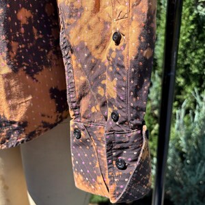 Puede incluir: Una camisa de manga larga marr&oacute;n y negra con un dise&ntilde;o estampado blanco y rosa. La camisa tiene un cuello abotonado y un cierre de botones en la parte delantera. La camisa est&aacute; hecha de una tela suave y c&oacute;moda.