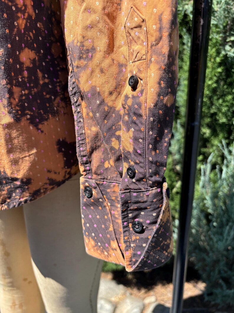 Puede incluir: Una camisa de manga larga marr&oacute;n y negra con un dise&ntilde;o estampado blanco y rosa. La camisa tiene un cuello abotonado y un cierre de botones en la parte delantera. La camisa est&aacute; hecha de una tela suave y c&oacute;moda.