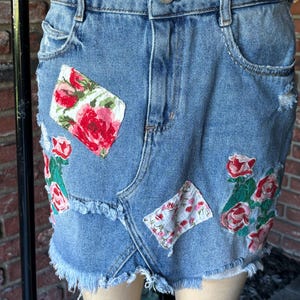 May include: A light blue denim skirt with floral patches and frayed edges. The skirt has a button closure and belt loops.