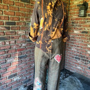 Puede incluir: Un pantal&oacute;n de cuadros marrones y beige con un parche en forma de coraz&oacute;n y un parche en forma de conejo. El pantal&oacute;n est&aacute; remangado en la parte inferior.