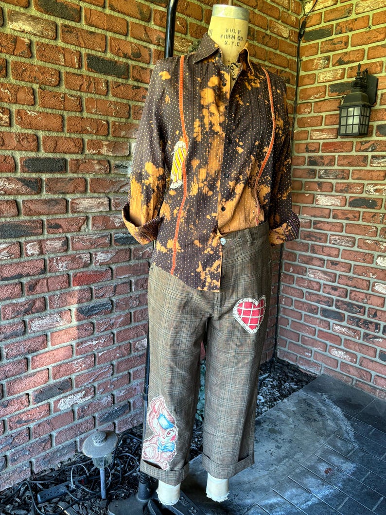 Puede incluir: Un pantal&oacute;n de cuadros marrones y beige con un parche en forma de coraz&oacute;n y un parche en forma de conejo. El pantal&oacute;n est&aacute; remangado en la parte inferior.