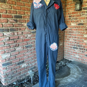 May include: A dark blue jumpsuit with three floral patches. The patches are in shades of red, blue, and white.