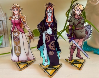 May include: Three acrylic character stands featuring a blonde woman in a pink and white dress, a blue woman in a black and blue dress, and a blonde woman in a green and brown dress. Each stand has a yellow triangular base with a black and yellow design.