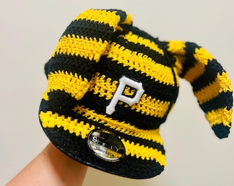 May include: A black and yellow striped crochet baseball cap with a white "P" logo. The cap has a curved brim and a "Snapback" label. The hat is handmade and features a unique, textured design.