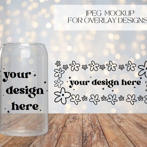 May include: A clear glass can with a black design that says "your design here" surrounded by small black flowers. The can is sitting on a wooden surface.