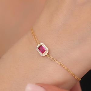 Könnte beinhalten: Ein goldenes Kettenarmband mit einem rechteckigen Rubin, der von einem Heiligenschein aus kleineren Diamanten umgeben ist.