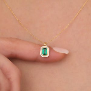 May include: A gold chain necklace with a green emerald pendant surrounded by small clear stones.