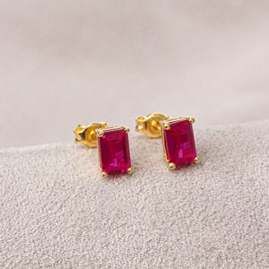 May include: A pair of gold earrings with red rectangular gemstones.