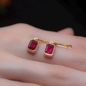 Puede incluir: Un par de pendientes de oro con piedras rectangulares rojas. Los pendientes son colgantes y tienen un diseño sencillo.