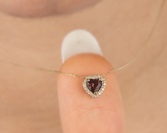 May include: A gold chain necklace with a heart-shaped pendant featuring a dark red gemstone surrounded by smaller clear gemstones.