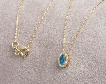 May include: A gold chain necklace with a blue oval pendant set in a gold halo with small clear stones.