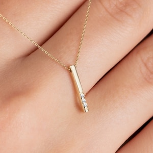 May include: A delicate gold necklace with a thin chain and a pendant shaped like a vertical bar with small diamonds set into it.