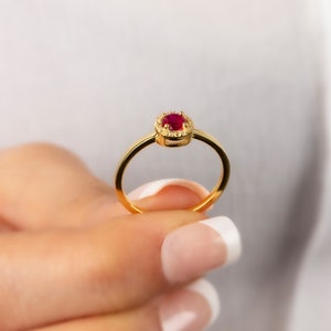 May include: A gold ring with a red gemstone surrounded by smaller white gemstones.