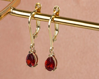May include: A pair of gold earrings with red teardrop-shaped gemstones.