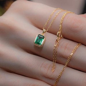 May include: A gold chain necklace with a green emerald pendant. The necklace is on a hand with white nail polish.