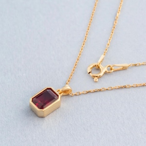 Puede incluir: Un collar de cadena de oro con un colgante que presenta una piedra rectangular roja.