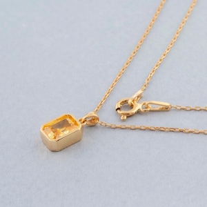 Könnte beinhalten: Eine goldene Kettenkette mit einem Anhänger mit einem rechteckigen, facettierten, gelben Edelstein.