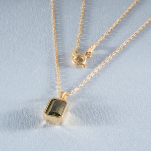 May include: A gold chain necklace with a green gemstone pendant. The pendant is a rectangular shape with a smooth, polished surface.