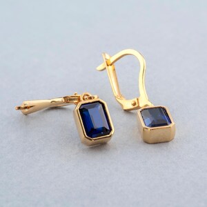 Peut inclure: Une paire de boucles d'oreilles en or avec des gouttes de pierres précieuses bleues. Les boucles d'oreilles ont un design simple et sont parfaites pour tous les jours.