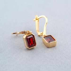 May include: A pair of gold earrings with red gemstone accents. The earrings have a simple, elegant design and are perfect for everyday wear.