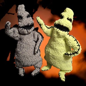 Pode incluir: Duas bonecas de crochê feitas à mão em forma de personagem. Uma boneca é cinza, a outra verde limão. Ambas têm detalhes costurados em preto, incluindo uma boca e braços costurados. O fundo é laranja e preto.