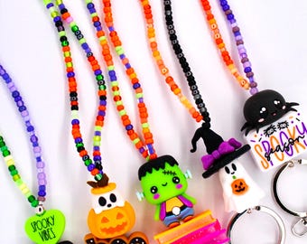 May include: Five beaded lanyards featuring Halloween-themed silicone charms including a ghost, a pumpkin, Frankenstein, a witch, and a spider. Each lanyard has colorful seed beads and a metal keyring with a lobster clasp and a small tassel.