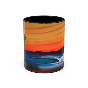 May include: A ceramic mug with a black interior and a wrap-around illustration of a sunset over a beach with a breaking wave. The sky transitions from orange to yellow, and the ocean is blue. A cactus is visible on the left side of the mug.