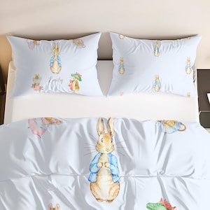 Puede incluir: Juego de cama blanco con ilustraciones de Peter Rabbit y sus amigos. El juego incluye dos fundas de almohada y una funda nórdica. Una funda de almohada tiene el nombre "Emily". Las ilustraciones son en tonos acuarela suaves.