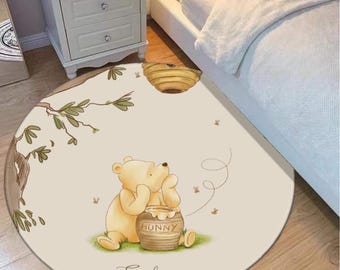 May include: A circular beige rug with a cartoon illustration of Winnie the Pooh and a honey pot. The rug includes a tree branch, a beehive, and the name "Emily". The rug is suitable for a child's bedroom and is made of soft material.