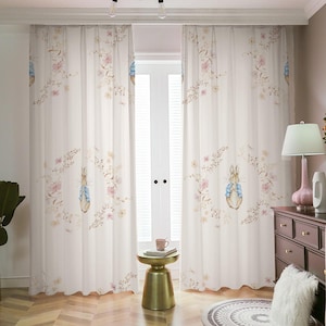 Puede incluir: Cortinas blancas y transparentes con un patrón floral y un diseño de Peter Rabbit. Las cortinas están colgadas de una barra blanca y están corridas hacia atrás para revelar una ventana con vista a una habitación.