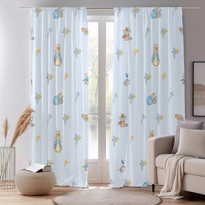 Pode incluir: Um par de cortinas brancas e transparentes com um fundo azul claro e um padrão repetido de personagens do Peter Rabbit, flores e outras criaturas da floresta. As cortinas estão penduradas em uma janela com vista para um lago e árvores.