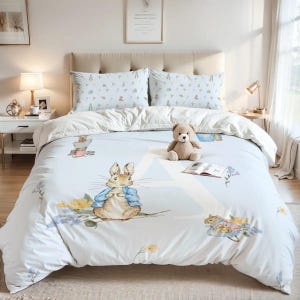 Puede incluir: Un juego de cama azul claro y blanco con un diseño de Peter Rabbit. El juego incluye una funda nórdica y dos fundas de almohada, con ilustraciones de Peter Rabbit, flores y otros personajes. Un oso de peluche y un libro abierto están en la cama.