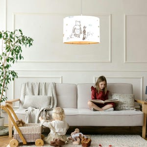 May include: A white ceiling lampshade with a Winnie the Pooh and Piglet design. The lampshade is hanging from a white ceiling in a living room with a white couch and two children playing on the floor.