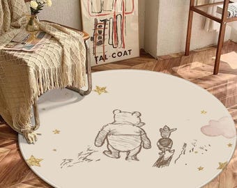 May include: A circular beige rug with a cartoon illustration of Winnie the Pooh and Piglet. The rug has a cream-coloured border and is decorated with gold stars and a pink cloud. The rug is placed on a wooden floor.