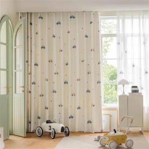 Könnte beinhalten: Cremefarbene Gardinen mit einem sich wiederholenden Muster aus kleinen blauen und grauen Autos. Die Vorhänge hängen vor einem Fenster, rechts ist ein durchsichtiger weißer Vorhang zu sehen. Der Raum wirkt hell und luftig.