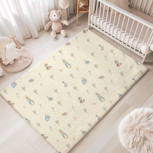May include: A rectangular area rug featuring a cream-colored background with a repeating pattern of small watercolor-style illustrations of rabbits in blue jackets and various tiny yellow and blue floral sprigs scattered across the surface.