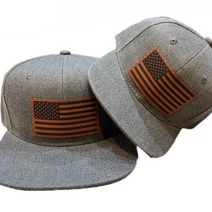 May include: Two grey baseball caps with a brown leather American flag patch on the front of each cap.