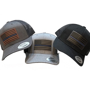 Op de afbeelding: Drie trucker caps met een leren Amerikaanse vlag patch met een dunne blauwe lijn. De caps zijn in grijs, zwart en grijs gemêleerd.