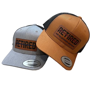 May include: Two baseball caps. One is grey with a brown patch that says "RETIRED". The other is brown with a black mesh back and a patch that says "RETIRED not my problem anymore". Both have curved peaks.